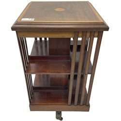 Edwardian inlaid mahogany revolving bookcase, square top with central fan inlay and satinwood banding with step moulded edge, upright splats and central square column supporting two tiers each with four divisions, on cruciform base with brass and ceramic castors