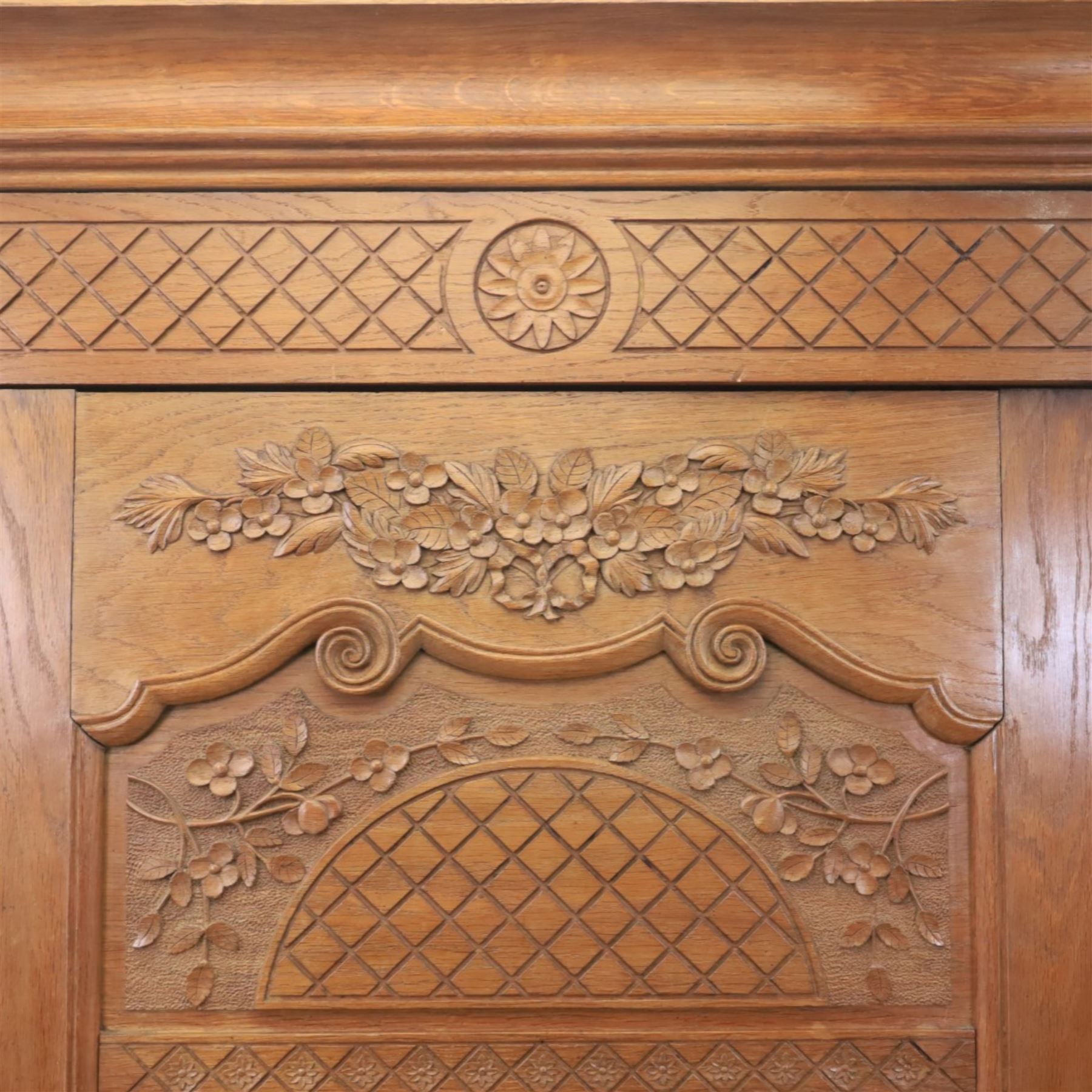 Early 20th century French oak triple door armoire, the moulded top above a frieze with carved lozenge decoration and central rosette, the central mirrored door enclosed by carved surround with floral crest, flanked by panelled doors with lattice carving, the base with shaped apron centred by carved basket motif, upon shaped cabriole supports