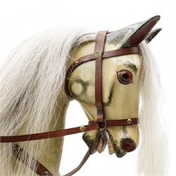 In the manner of F. H. Ayres - large carved wooden rocking horse, in dapple grey paint finish, decorated with glass eyes, leather reins, stirrup and saddle, on bowed rockers united by turned stretchers and boarded base 
