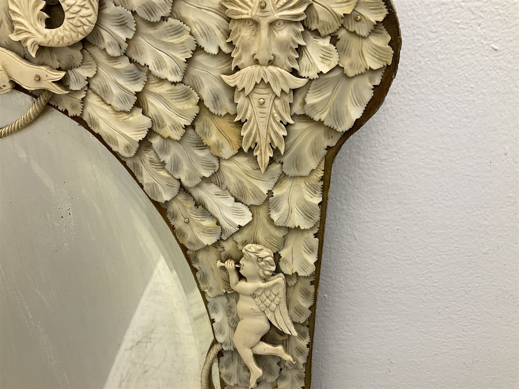 Pair 19th century French Dieppe bone and ivory wall mirrors, the oval bevelled mirror plates within rectangular frames with shaped tops, profusely decorated with ivory leaves, further detailed with carved bone armorial type crest inscribed 'SGOTORVM', putti, fish and mask heads, H81cm W48cm