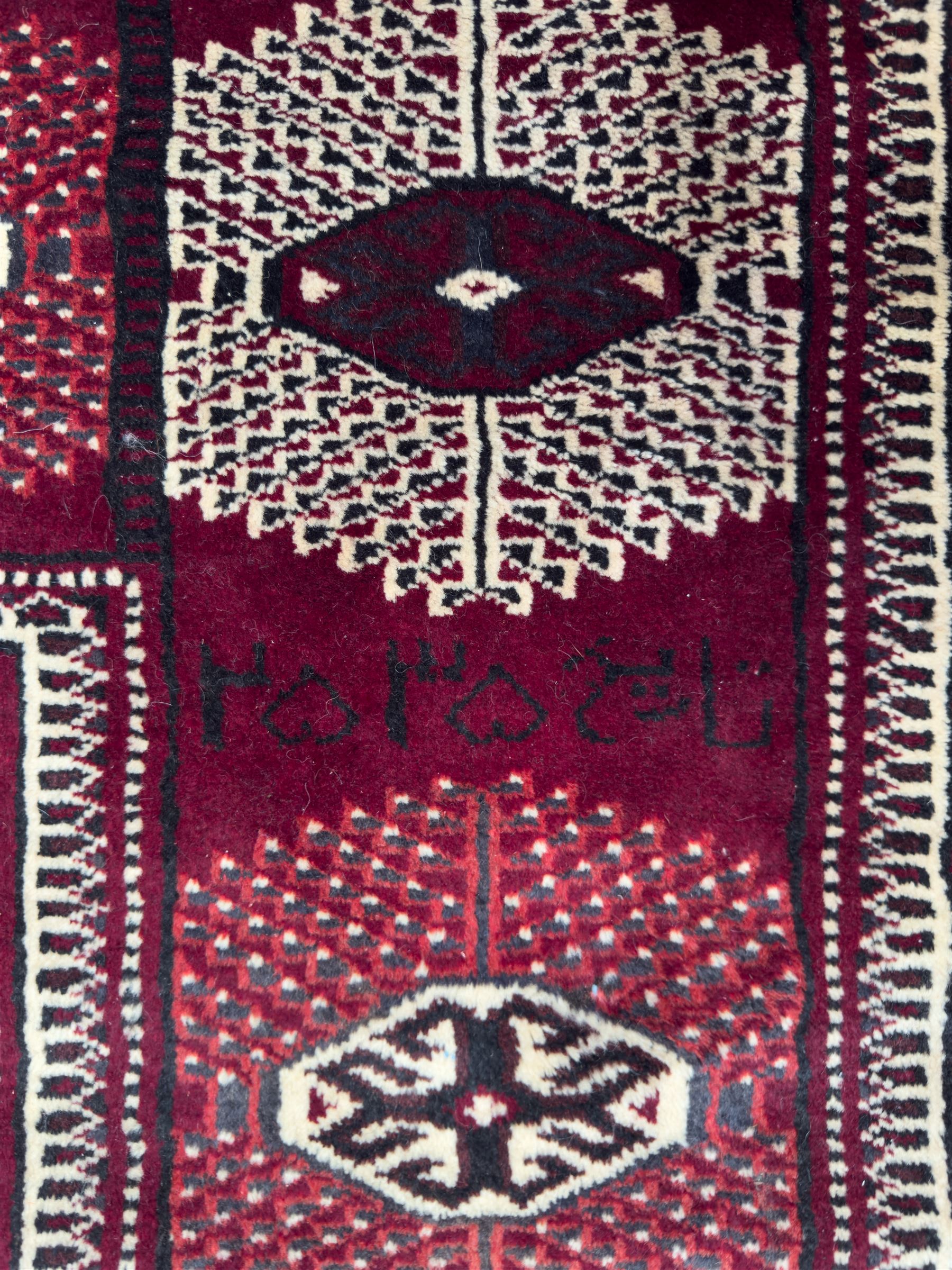 Northeastern Persian Yamut  hand-knotted carpet, the rich burgundy field with repeating rows of stepped gul motifs in cream and black, enclosed by multiple linear and geometric borders with hooked motifs and diamond medallions