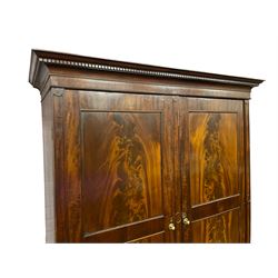 George III mahogany double wardrobe, the projecting cornice with dentil moulding over two panelled doors with mirror-lined interiors, enclosing hanging rails and brass hooks, the base fitted with two drawers, raised on bracket feet