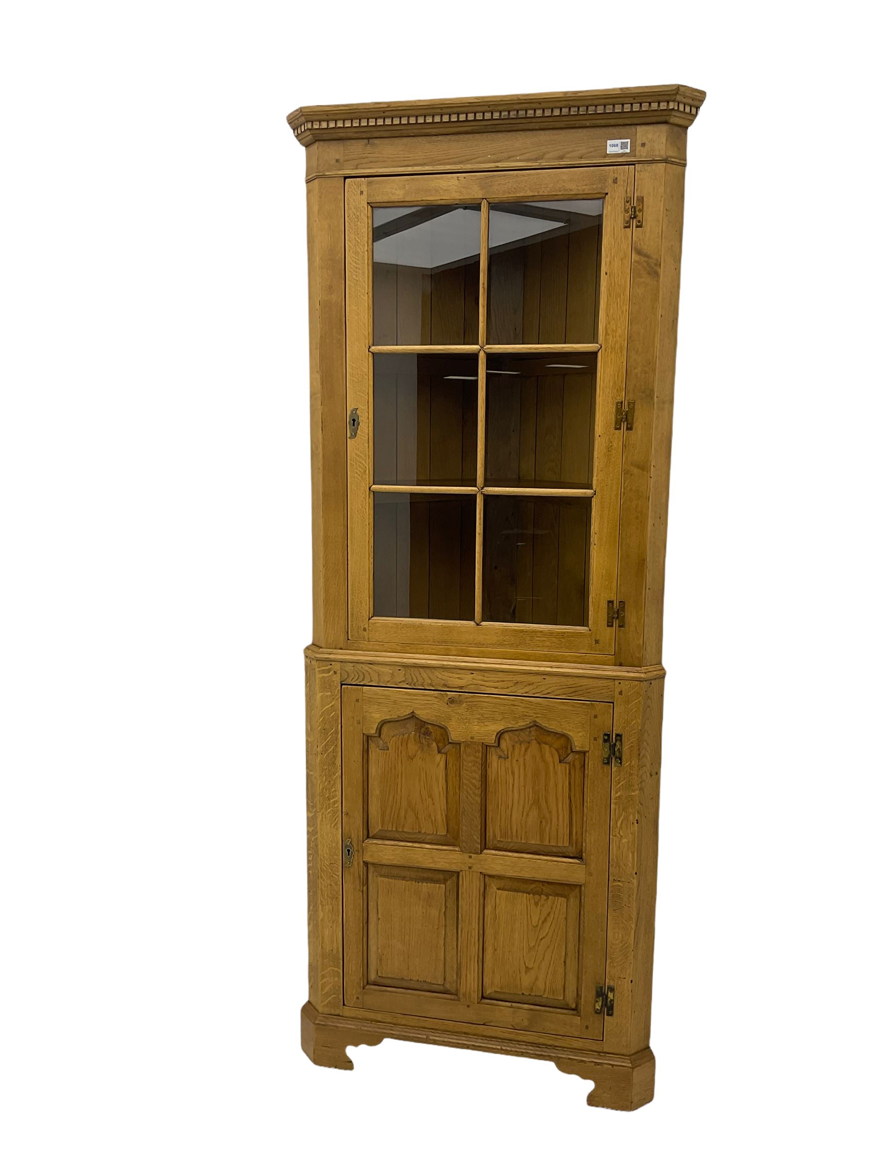 Traditional light oak corner cabinet, projecting cornice, dentil frieze, single glazed door above single fielded door