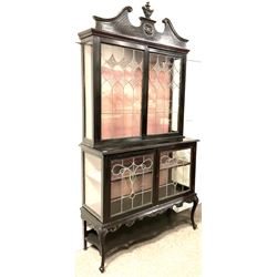 Late 19th century mahogany Empire style display cabinet, swan neck pediment and carved urn finial over two lead glazed doors enclosing two shelves, two glazed doors under, raised on cabriole front supports
