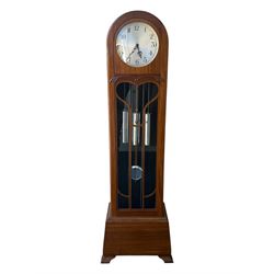 English- Art deco mahogany 8-day longcase clock, with an arched top and fill length fully glazed door beneath, on a short plinth with bracket feet, three train chain driven movement with visible stainless steel cased weights and pendulum, silvered dial with Arabic numerals, minute track and pierced steel hands, quarter chiming movement with  Westminster/ Whittington/ strike/silent selection.
