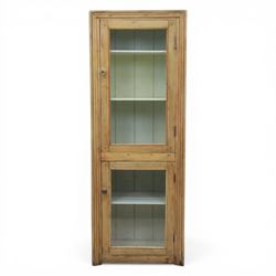 Early 20th century waxed pine kitchen cupboard, rectangular form with moulded top, enclosed by two glazed doors revealing painted interior with shelves, boarded sides and back, fitted with brass knob handles