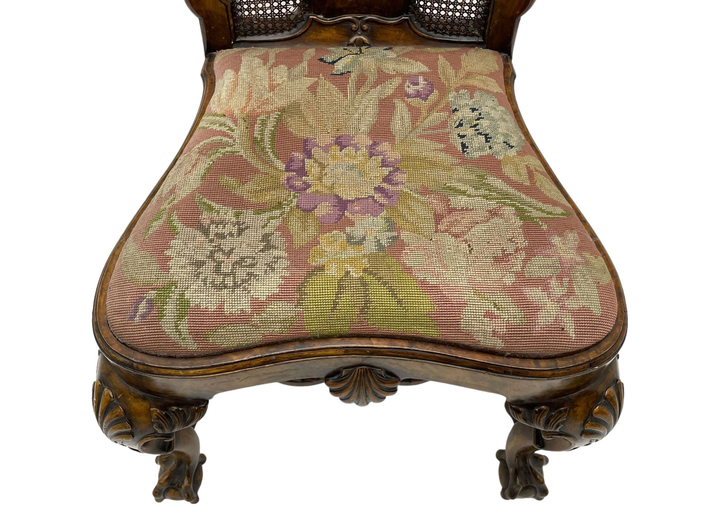 Pair of early 20th century Queen Anne design chairs, the cresting rail carved with scroll and central shell motif, shaped uprights and splat encased in cane work panels, shaped moulded seat frame with shell motif, floral needlework upholstered drop-in seat cushion, on shell carved cabriole supports with ball and claw feet, united by turned and shaped middle stretcher carved with acanthus leaf