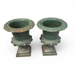 Pair of Victorian cast iron campana garden urns, the flared rim with repeating stylised anthemion motifs with scrollwork, over a deep gadrooned and Aesthetic moulded underbelly, fluted and foliate lower bowls on square pedestal bases, in antique green-painted finish