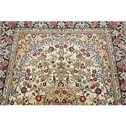 Central Persian Kashan hand-knotted carpet, ivory ground with a central floral medallion with an all-over design of scrolling vinery, palmettes, and flowering sprays i tones of madder red, cobalt, navy blue and sage green, with conforming spandrels, main border of deep indigo ground with repeating palmettes and stylized floral heads, flanked by narrow guard stripes, with cotton fringe ends, with cotton fringe ends 