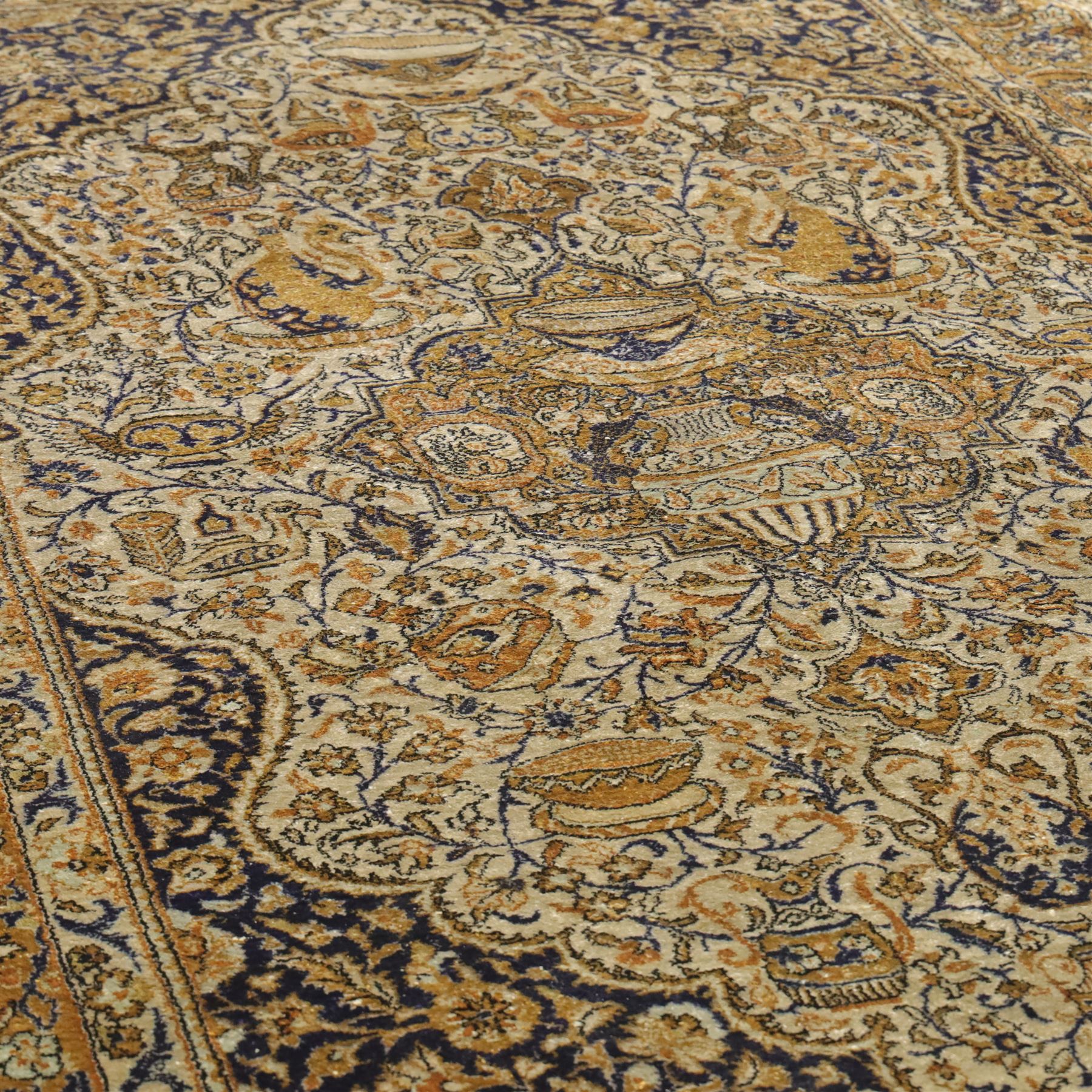 Persian Kashan design silk and wool blended rug, with a central medallion incorporating vases and scrolling floral motifs, set against a dark blue and ivory ground within a patterned border, some fraying to end fringes