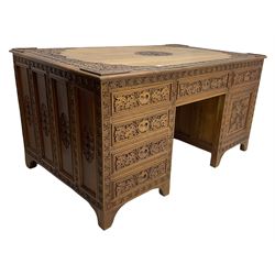 Large Indian hardwood twin pedestal desk, heavily carved with foliate decoration, one side fitted with two drawers and the other fitted with six drawers and cupboard,