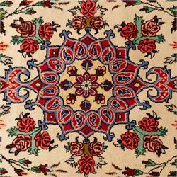 Two small rugs, an ivory ground example decorated with a central floral medallion and scattered rose sprays, enclosed by a navy foliate border (62cm x 101cm), and a crimson pictorial mat worked with seated figures, an animal and birds amongst flowering plants (45cm x 79cm) (2)
