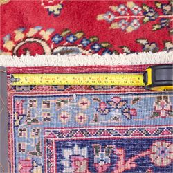 North East Persian Meshed hand-knotted rug, madder red field with central multi-lobbed medallion in shades of indigo, ivory, and sofa pastel tones surrounded by scrolling floral vines, palmettes, stylized blossoms, floral sprays, and cartouches, framed by Indigo spandrels, enclosed within a broad dark blue main border, flanked by multiple narrow guard stripes, with fringe ends 