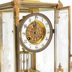 French- Art-deco Edwardian 8-day four-glass clock garniture, with etched glass panels, cast brass decoration to the corners of the case and splayed feet representing cloven hoofs to the base, case surmounted by a large oval urn on a tiered brass platform, two part dial with a recessed brass centre comprising of pierced radial decoration, with steel spade hands and Arabic numerals to the chapter, rack striking movement with a deadbeat Brocot escapement, striking the hours and half-hours on a bell. With a visible twin file mercury pendulum. Garni comprising two large twin handled urns on rectangular pedestals raised on conforming feet representing cloven hoofs, Clock and garni presented on three shaped wooden gesso bases with velvet pads. With key.