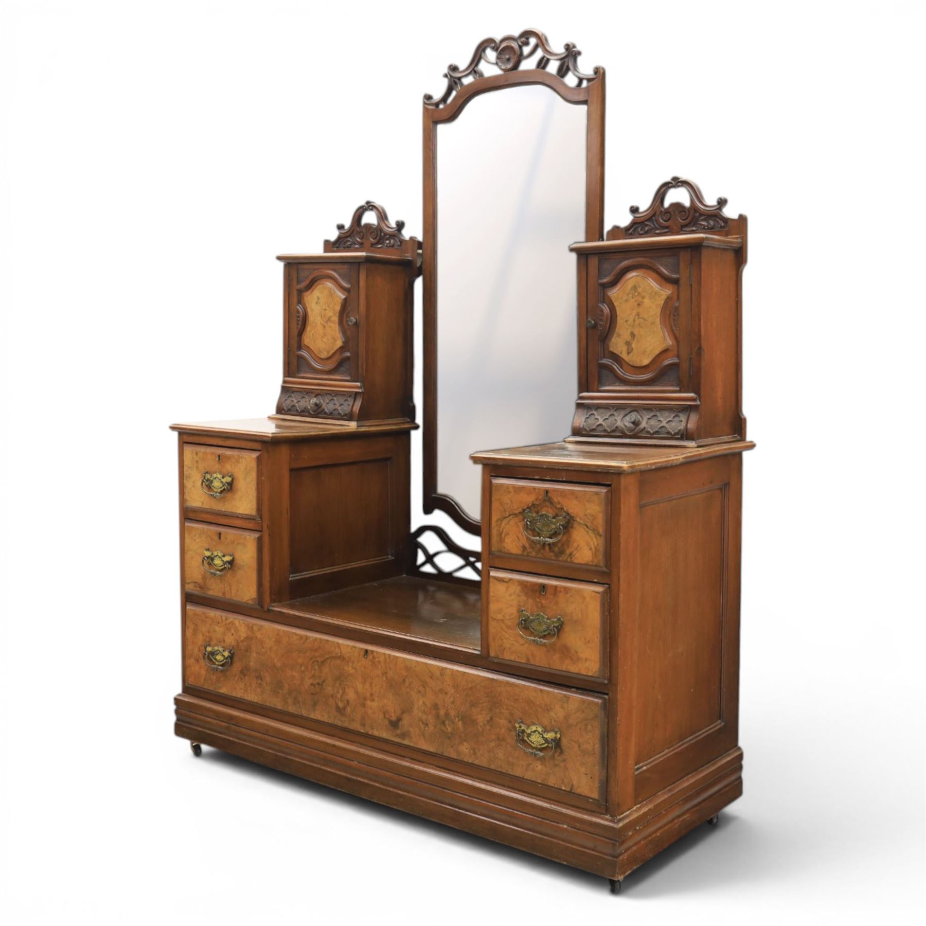 Edwardian figured walnut dressing chest, with central tilting mirror with pierced fret work, flanked by cabinet with figured walnut panelled door above a trinket drawer, with four short over a long long drawer, raised on a plinth base with castors 
