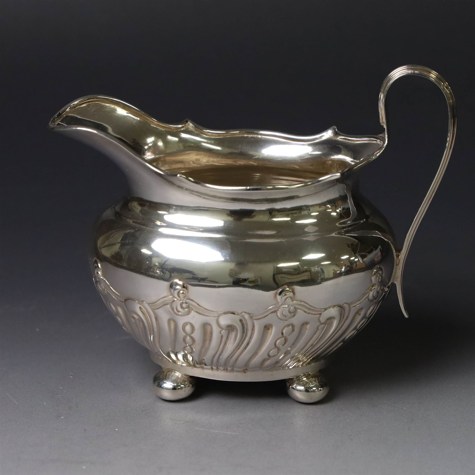 Edwardian silver three piece tea service, comprising teapot, twin handled open sucrier and a cream jug, each of oval form with embossed scrolling decoration and upon four bun feet, the teapot with ebonised wooden handle and finial, hallmarked Thomas Bradbury & Sons Ltd, Sheffield 1903, teapot H16cm