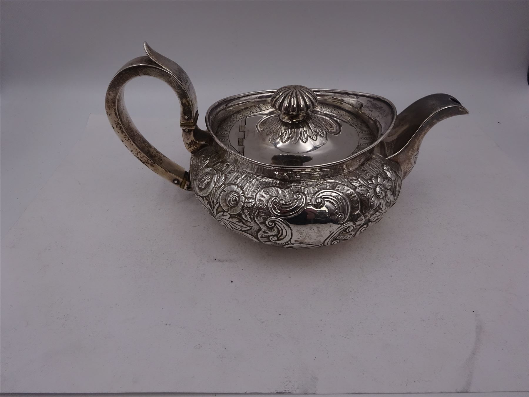 George III Irish silver teapot, of squat circular form, the body with repousse and chased floral and C scroll decoration, with capped C handle and ivory insulators, engraved to base 'Presented to Troop Sergeant Major John Percival, of the 4th Dragoon Guards by Alex D. Tait, Esq, late Captain in that corps as a mark of approbation of his steady and upright conduct when Sergeant Major of his Troop, Dublin, June 2nd 1843', hallmarked William Law, Dublin 1817, H12.5cm, This item has been registered for sale under Section 10 of the APHA Ivory Act