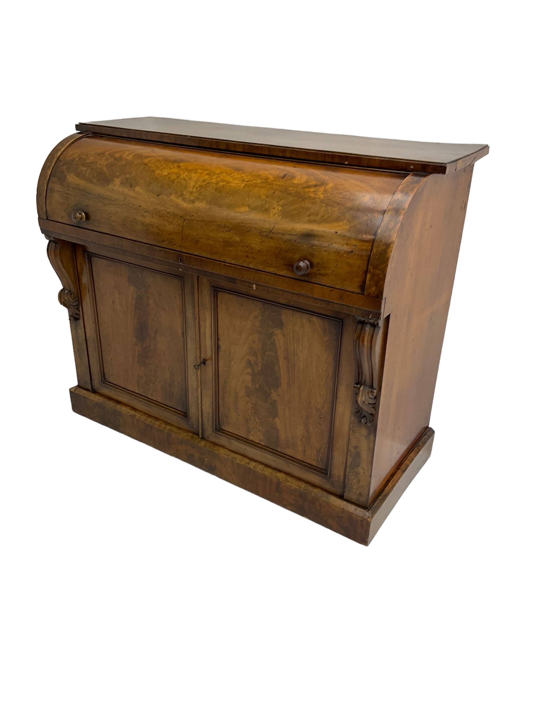 Victorian mahogany roll-top writing desk, top concealing fitted interior with pigeonholes and three drawers, the trisector inset writing surface with writing slope, base fitted with panelled cupboard enclosing single shelf, decorated with scrolled corbels