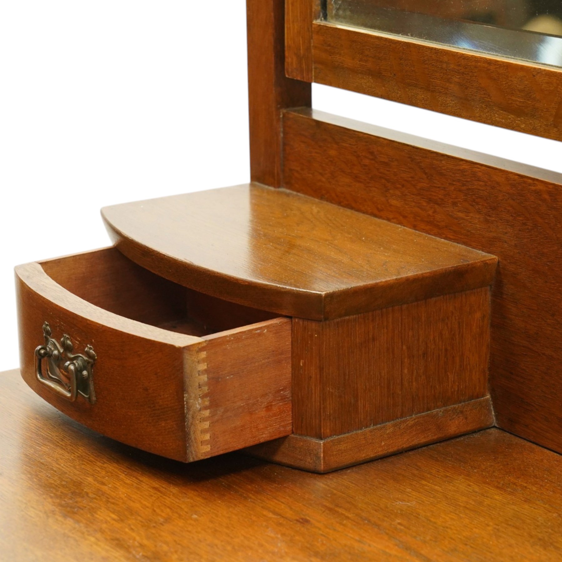 Manner of Liberty & Co. - Arts & Crafts oak dressing chest, the arched swing mirror with roundel-carved frieze and bevelled plate, serpentine-front top with two raised trinket drawers, fitted with two drawers with brass Art-Nouveau poppy handle-plates, on square tapering supports with castors