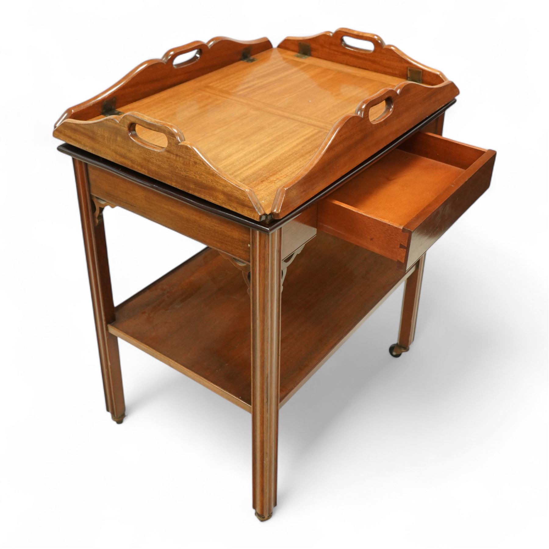 20th century mahogany butler’s tray on stand, with folding gallery tray top featuring shaped hand grips and brass hinges, fitted with single drawer and lower shelf, on square section legs with pierced brackets and castors