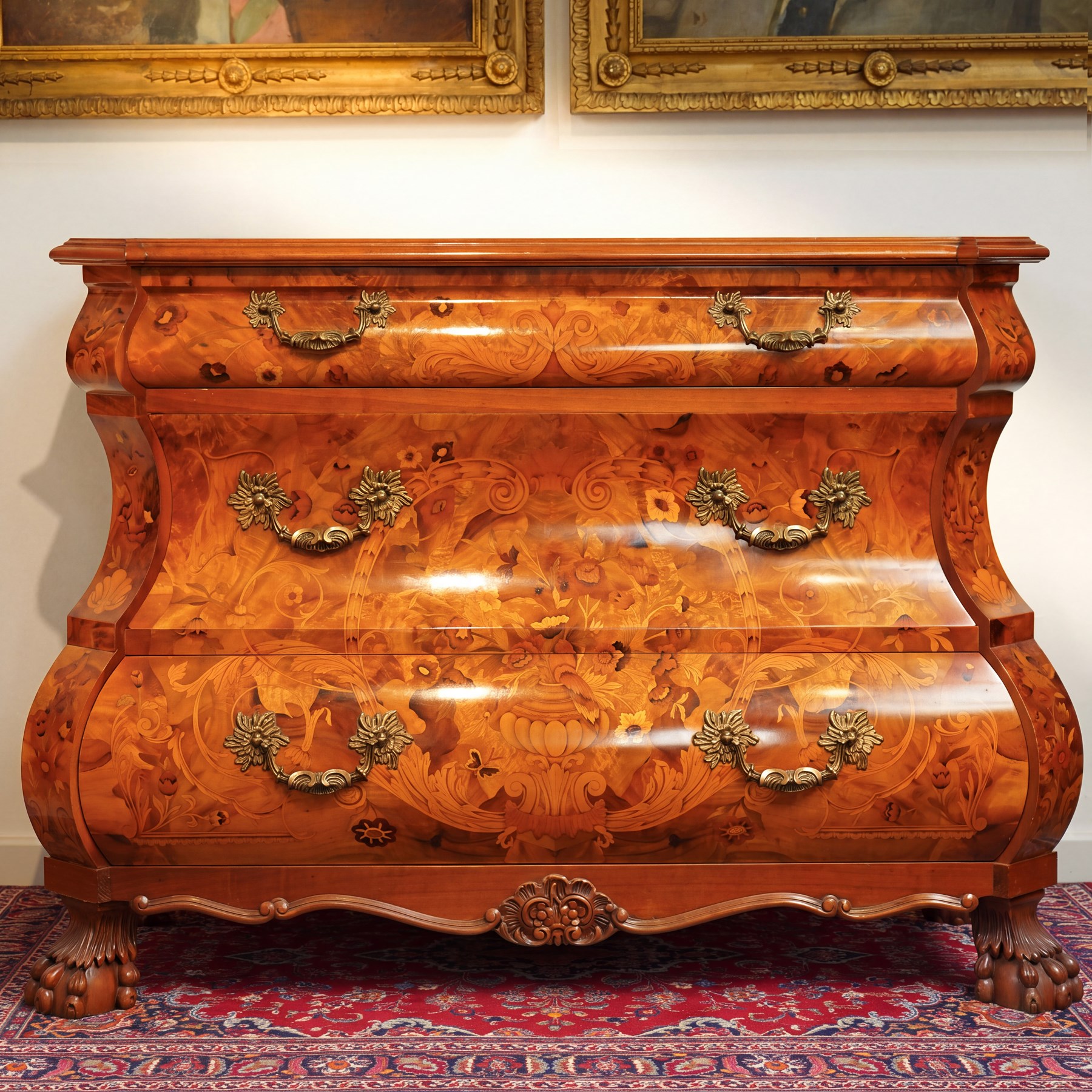 Colombo Mobili - Italian walnut and floral marquetry bombé commode chest, rectangular top with canted eared corners inlaid with urn motif and trailing scrolling foliage, fitted with three long graduating drawers with gilt metal handles, profusely inlaid with scrolling acanthus leaves interspersed with urns and cartouches, on large carved ball-and-claw feet