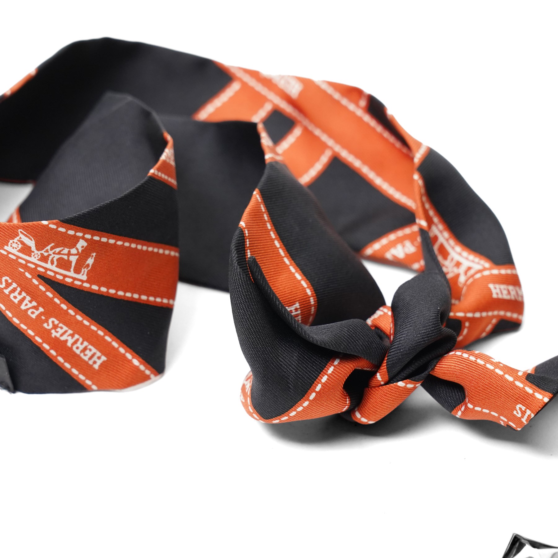 Hermès - two ‘Bolduc’ silk Twilly scarves, in orange/black and navy/brown colourways, together with three palladium-tone Médor pyramid Twilly scarf rings, with original dust bag and cylindrical box