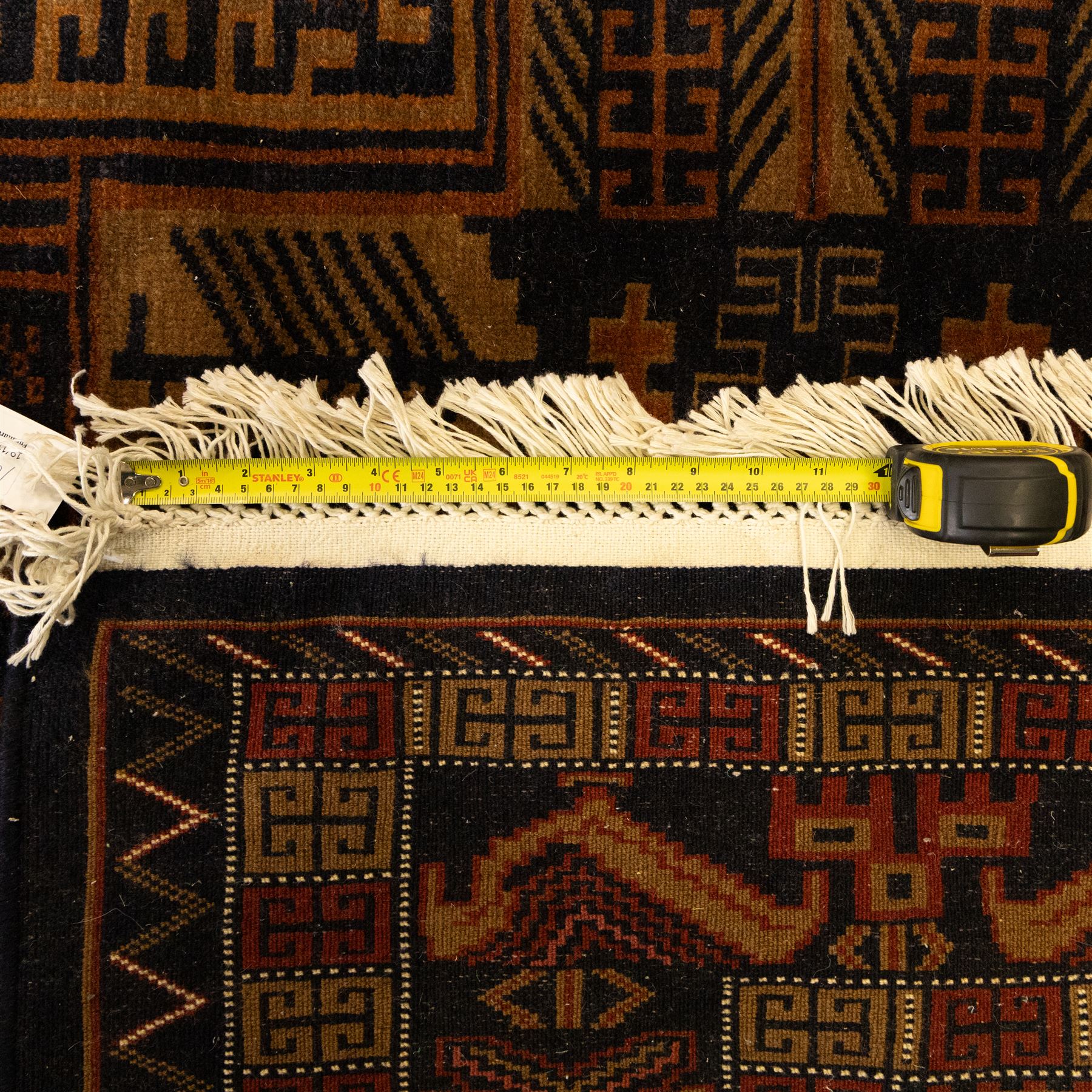 Baluch tribal style rug, dark indigo field with rows of linked gul and angular medallions in madder, camel, and ivory tones, within multiple geometric borders, including the main border of stylised animals