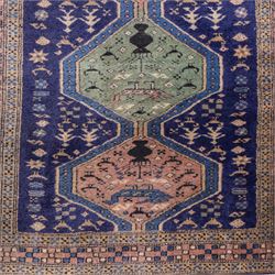 North West Persian Ardebil hand-knotted runner, indigo field composed of a vertical series of large linked hexagonal medallions alternating soft terracotta and sage-green grounds, medallions connected narrow waist panels, surround field filled with geometric devices on a pale blue ground, principal border decorated with a repeating geometric and floral motif on a light ground flanked by narrow guard stripes incorporating small rosettes, with cotton fringe ends 