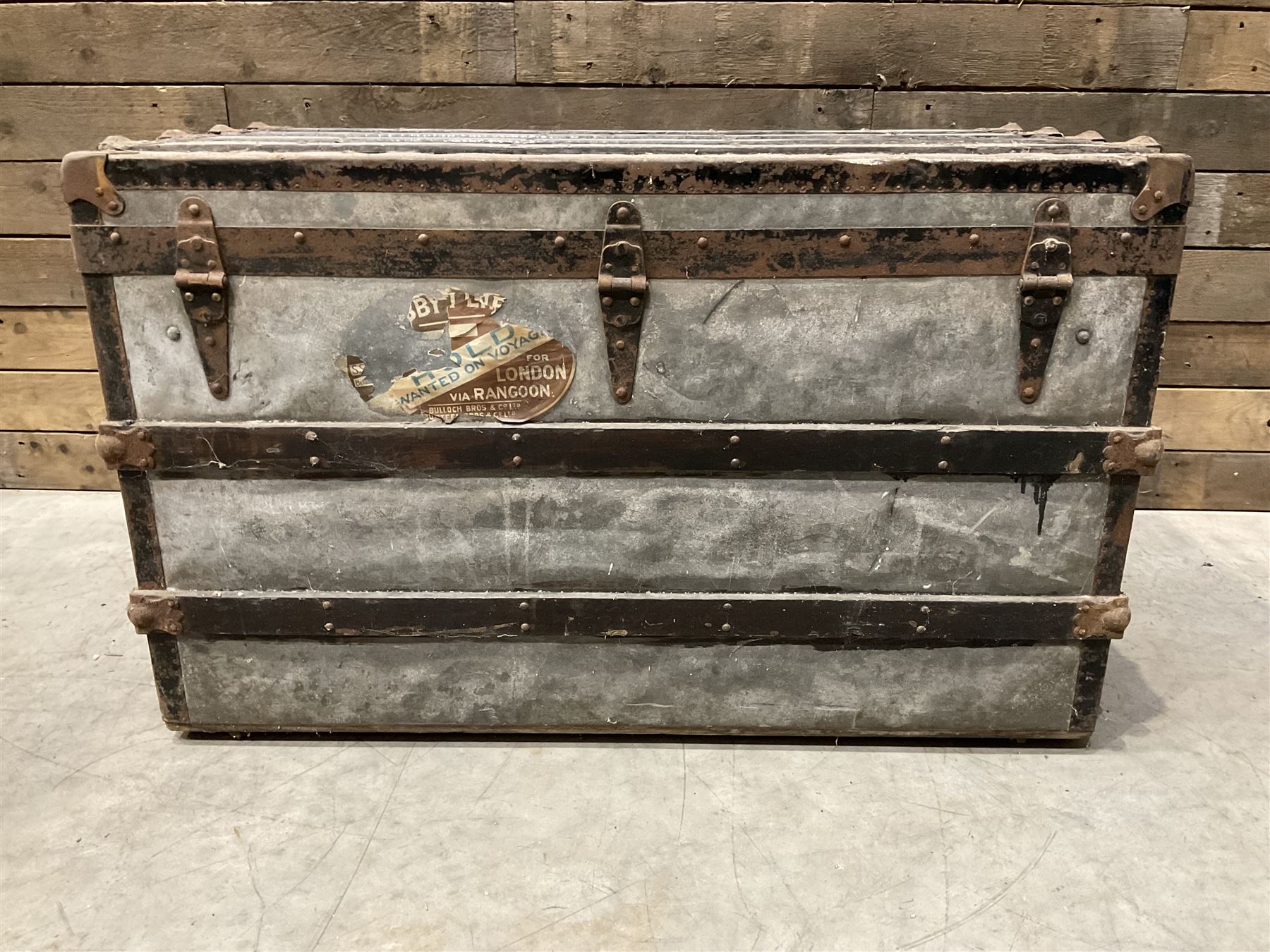 Early 20th century wood and metal bound zinc travelling trunk, hinged top with three clasps, decorated with period luggage labels