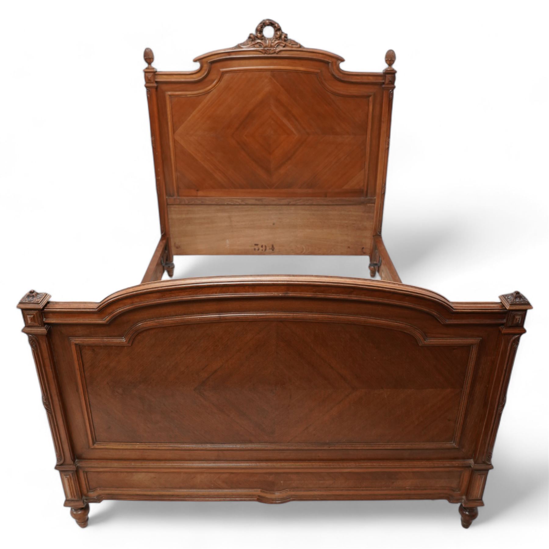 20th century French walnut 4' 6'' double bedstead, the headboard with flower head wreath pediment flanked by carved pineapple finials, reed and ribbon carved corner uprights, quarter-matched veneers, on turned feet, together with upholstered bed base