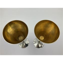 Pair of modern silver goblets by Stuart Devlin, the tapering cylindrical bowls each with spot hammered decoration and gilt interiors, the parcel gilt stems with signature textured detailing and six graduating knops, upon conforming spreading circular foot, hallmarked Stuart Devlin, London 1976, H17.7cm