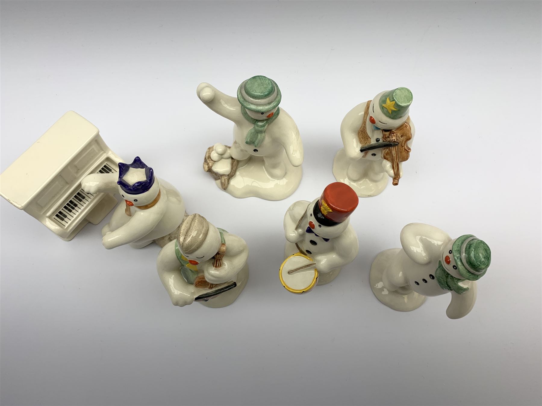 Royal Doulton The Snowman Gift Collection snowman band figures, comprising Cellist Snowman DS17, Violinist Snowman DS11, Drummer Snowman DS15, and Pianist Snowman DS12, plus Snowman's Piano DS13, together with two further figures The Snowman DS2, and The Snowman Snowballing DS22. (7). 