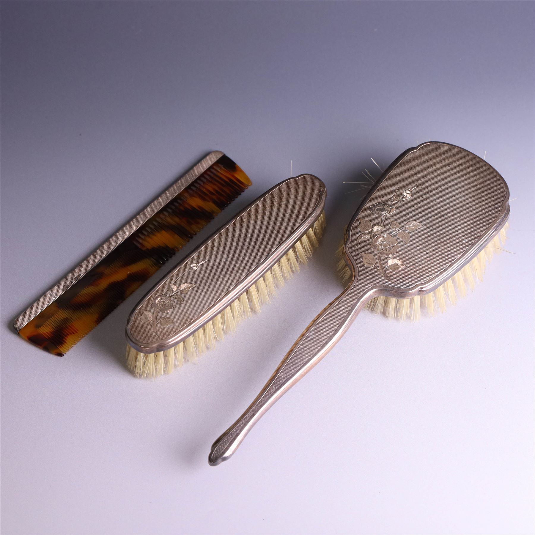20th Century silver mounted dressing table set, comprising hand mirror, clothes brush, hairbrush and comb holder, each with engine turned and engraved floral decoration, three pieces hallmarked Adie Brothers Ltd Birmingham 1964, the comb holder hallmarked Elkington & Co Ltd Birmingham 1965, contained within a fitted tooled leather case
