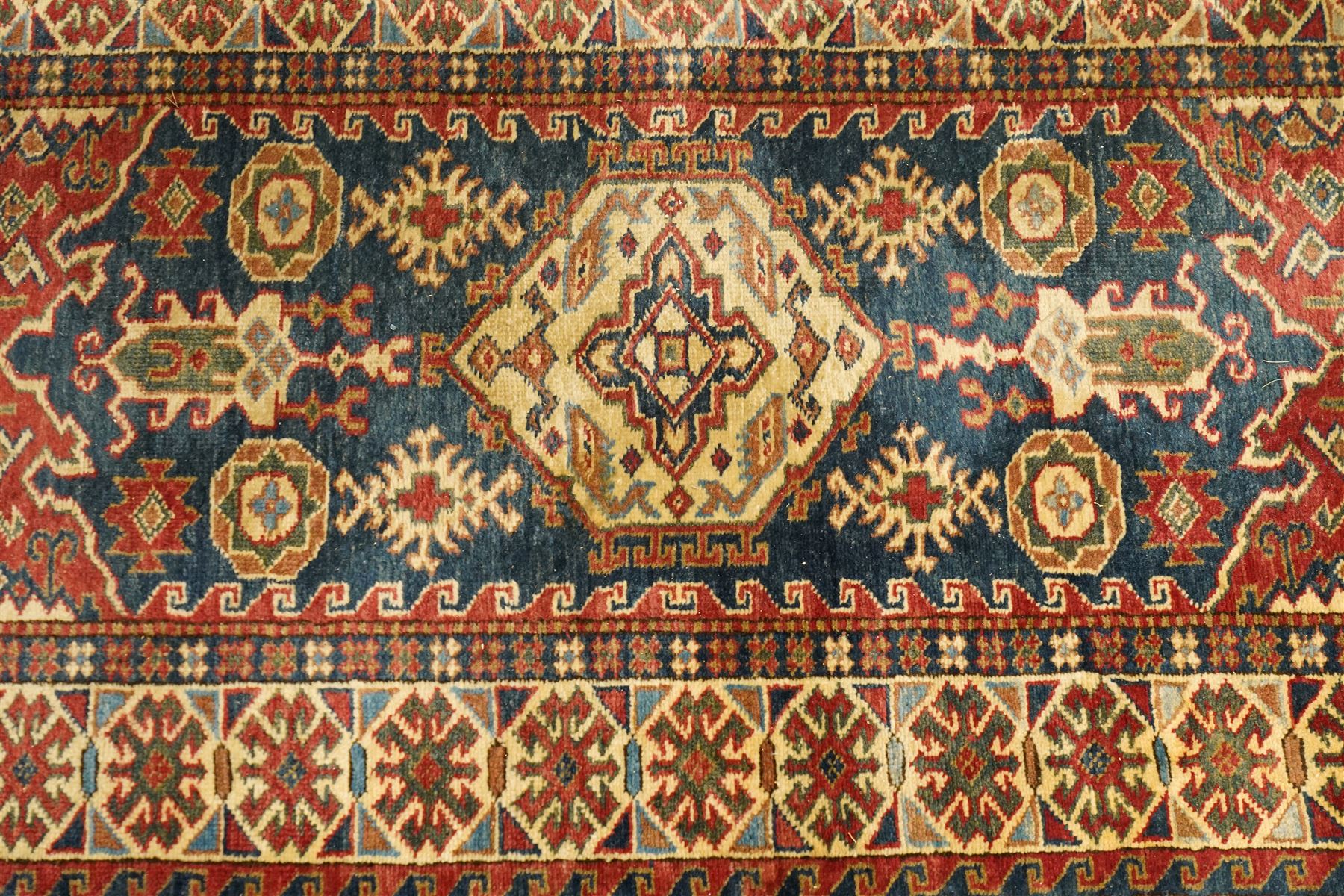Caucasian hand-knotted runner, dark navy ground with three ivory geometric medallions surrounded by stylised flowerheads and angular motifs in madder red, green and ivory, enclosed by repeating geometric borders