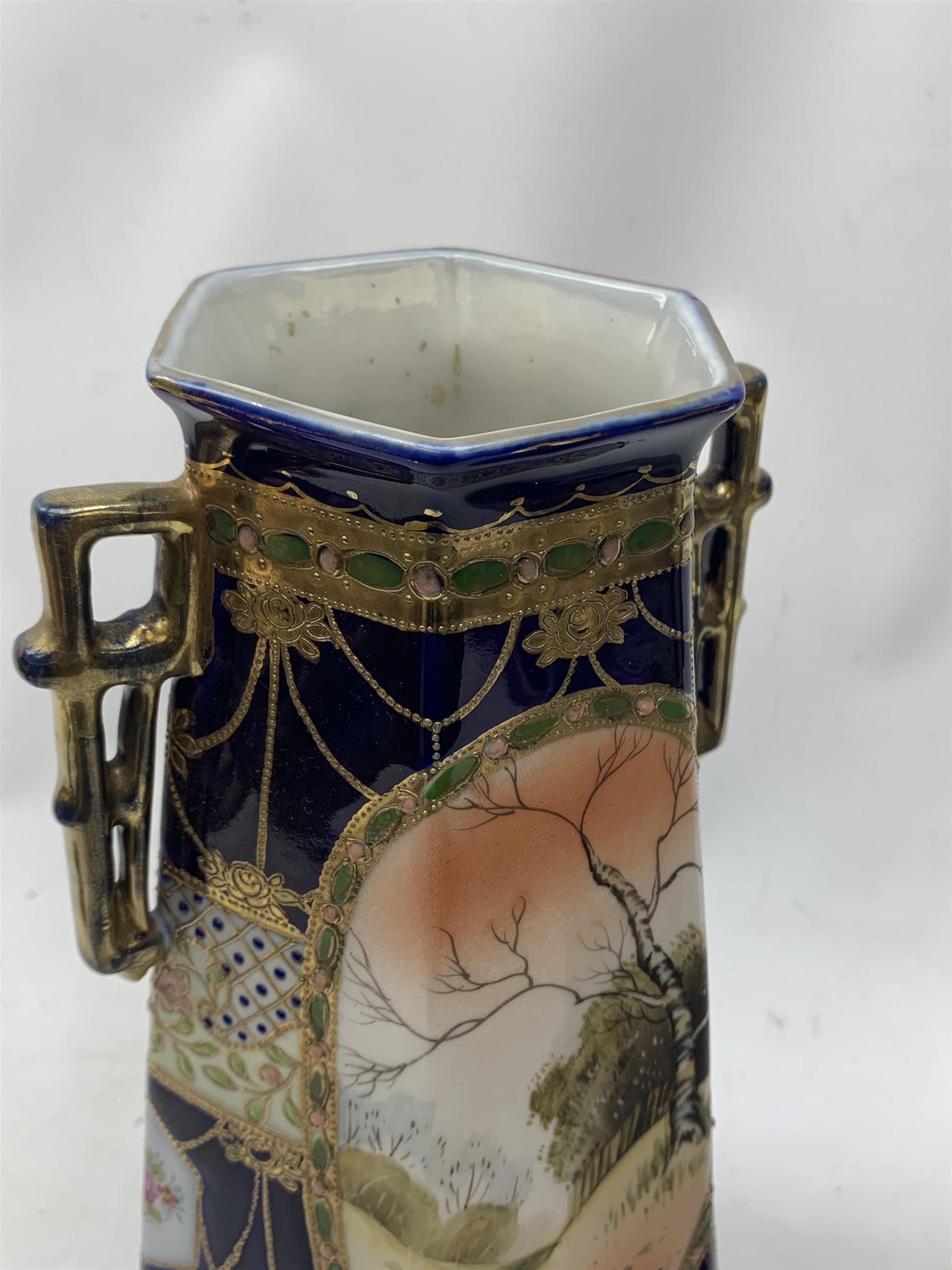 A pair of Japanese Nippon Kinjo vases, of tapering hexagonal form with twin stylised handles, the cobalt blue ground with oval hand painted panels to front and verso depicting landscapes, further detailed with smaller floral bands and panels and heightened with gilt, each with mark beneath, H30.5cm.  