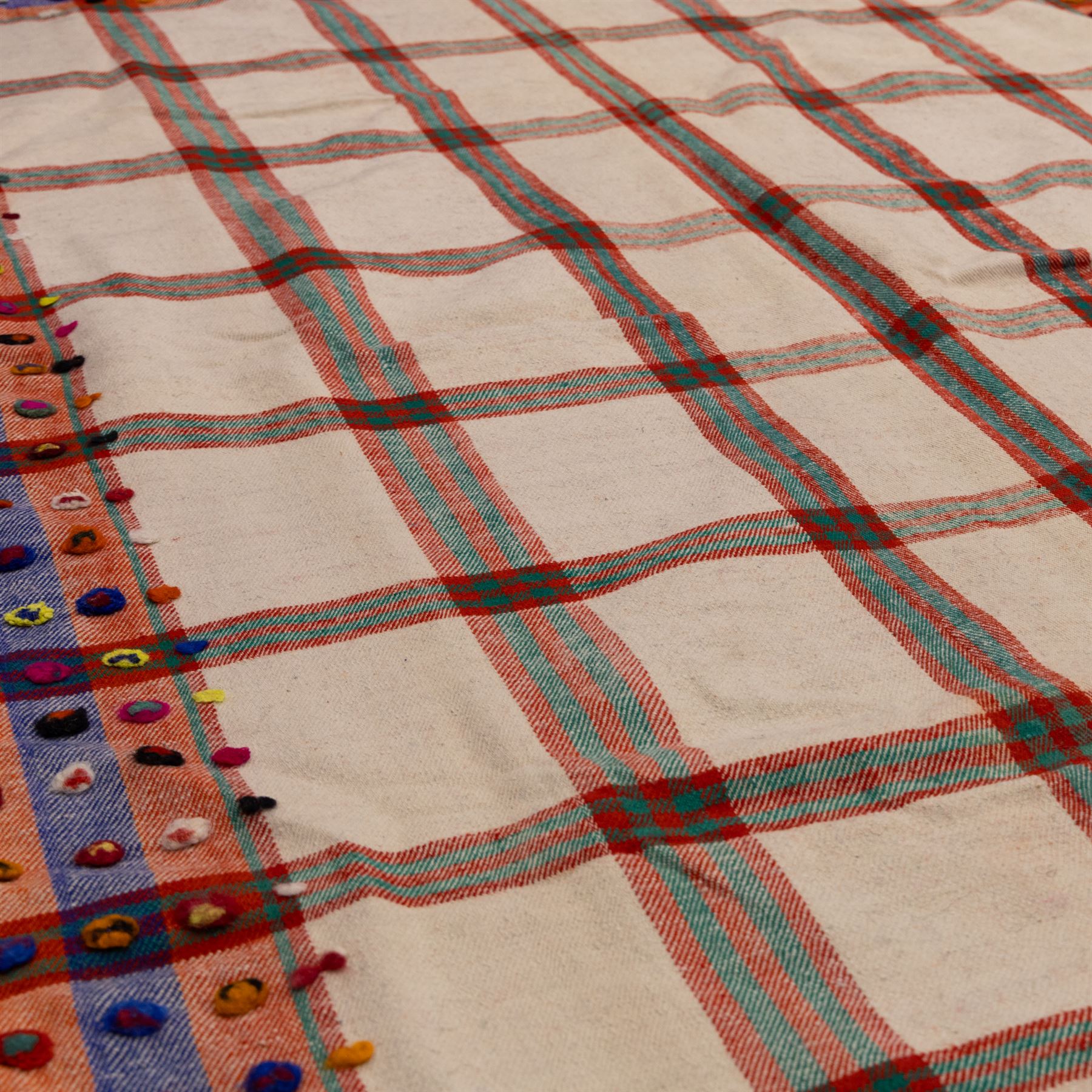 South West Persian Jajim flatweave kilim, ivory ground, woven with a bold checked and striped design in red and green, bordered by wide geometric polychromed bands decorated with circular tufts 