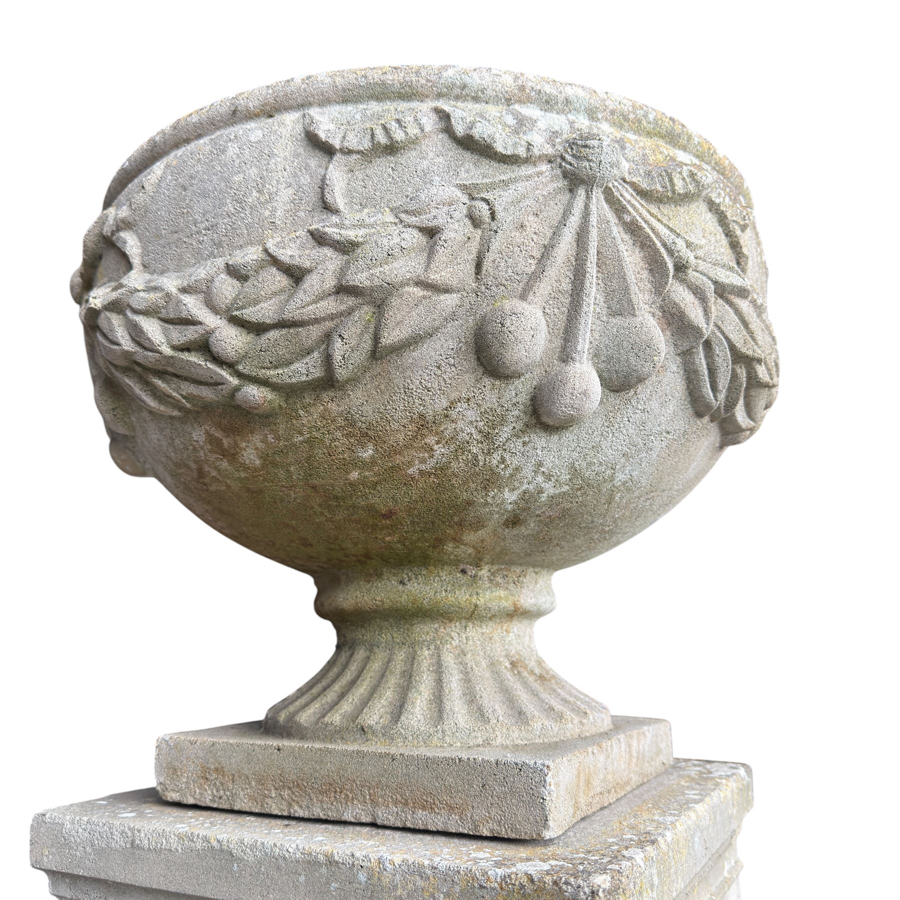 Pair of quality Neoclassical design Haddonstone cast stone garden urns, the globular  body decorated with relief foliate festoons and fruiting motifs, over a fluted socle, the rectangular pedestals with relief foliate wreaths and ribbon garlands