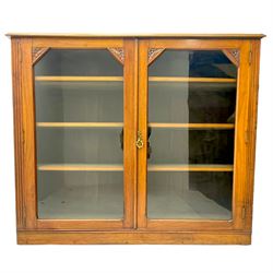 Edwardian walnut bookcase display cabinet, fitted with two glazed doors enclosing six adjustable shelves, flanked by floral carved corners and fluted uprights 