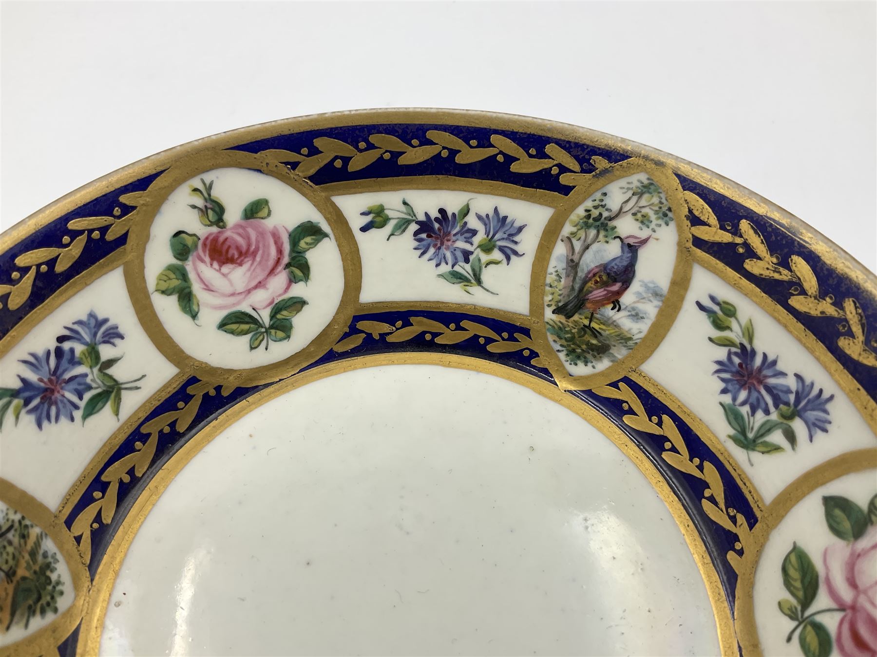 19th Sèvres style porcelain cup and saucer, the cup painted with a figural scene, against a scalloped border of scrolling floral swags on a blue ground, together with a Sèvres soft paste porcelain coffee can and saucer, painted with panels of exotic birds, roses and a border of cornflowers, LL monogram enclosing date letters H above painters mark, coffee can H6.5cm, saucer D13.5cm (2)