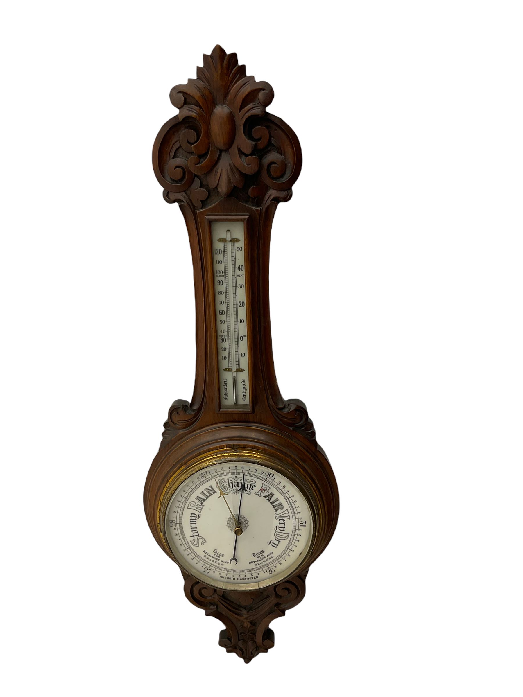 An English 1930’s solid oak carved hall barometer in a scroll shaped carved case with relief carving, aneroid movement, 8” white register measuring barometric air pressure from twenty-six to thirty-one point nine inches, weather predictions in black upper and lower case gothic script with a blue steel indicating hand and brass recording hand, brass dial bezel with flat bevelled glass, mercury thermometer enclosed in a glazed rectangular box displaying temperature in degrees Fahrenheit and Celsius on a white register. H87cm


