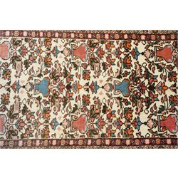Iranian Persian style rug, repeated stylised vase and floral motifs arranged symmetrically across a ivory field, framed by red main border