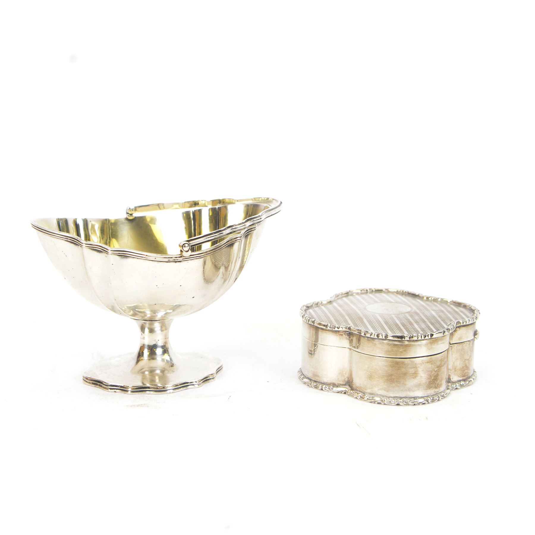 Early 20th century silver trinket box, of quatrefoil form, with shaped rim and engine turned decoration to cover, with vacant circular cartouche, hallmarked Deakin & Francis, Birmingham 1917 or 1942, H3cm, W8.5cm, together with an early 20th century silver swing handled sugar basket, with gilt interior, hallmarked Levi & Salaman, Birmingham 1918