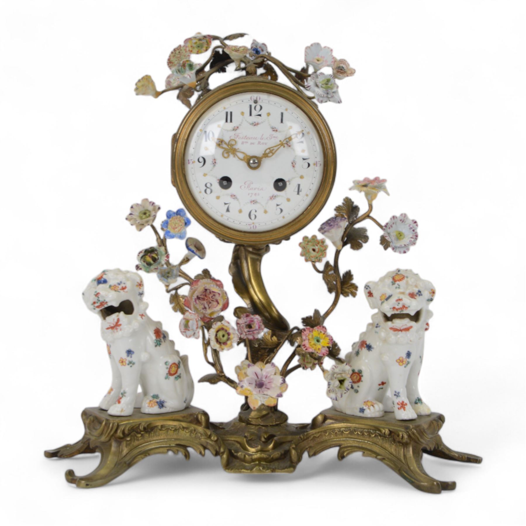 French- early 20th century 8-day Chinoiserie brass and porcelain mantel clock in the 18th century style, brass base with splayed feet profusely decorated with clusters of painted porcelain flowers and two decoratively painted Chinese foo dogs, movement enclosed in a circular porcelain movement case illustrated with birds of paradise and oriental motifs, with a white enamel dial Arabic numerals, minute markers, pierced gilt hands and a floral swag, rack striking Parisian movement striking the hours and half-hours on a bell. With a visible sunburst pendulum and key.