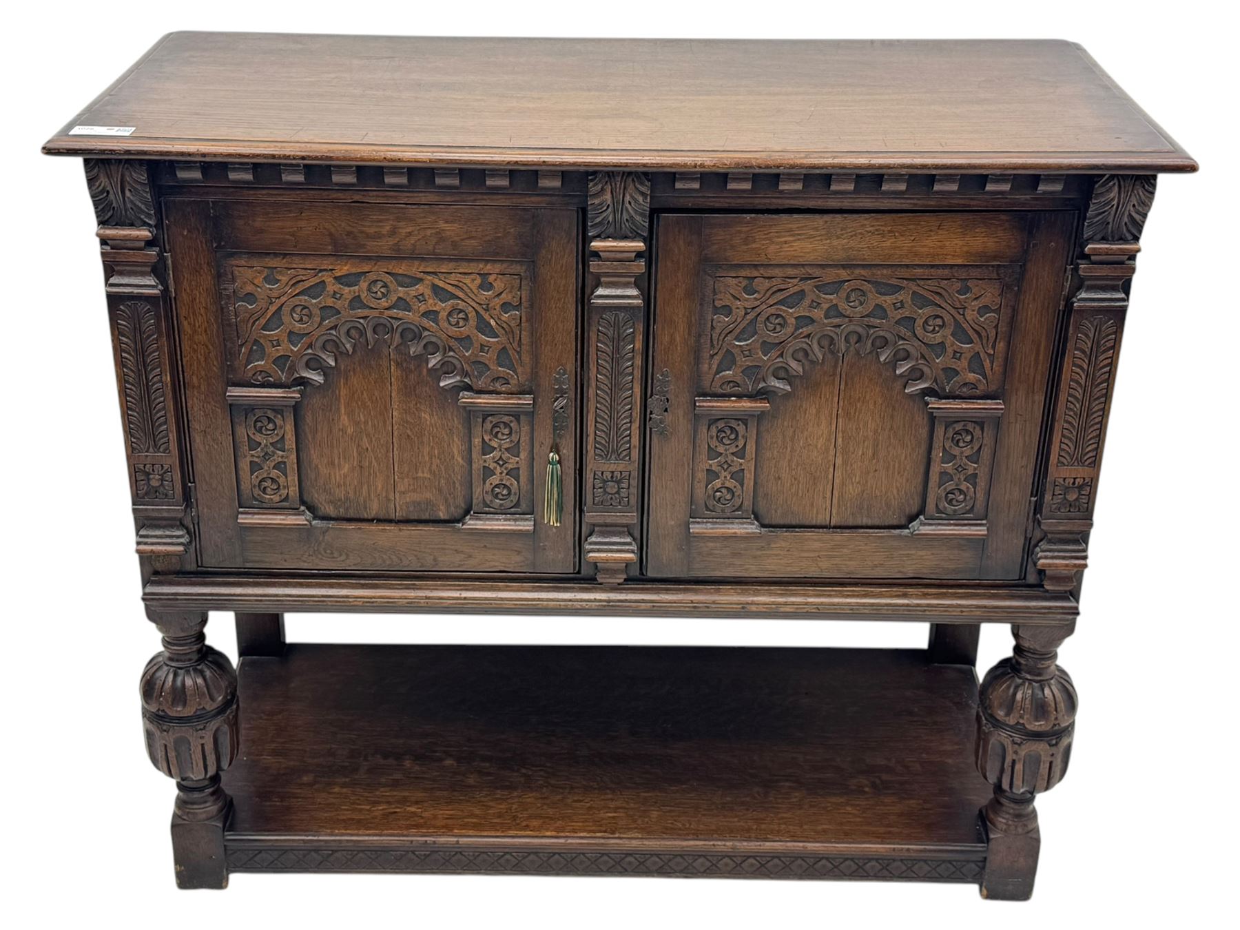 Jacobean design carved oak two door cupboard, the frieze and twin cupboard doors carved with arcaded panels and stylised foliage, raised on baluster supports united by an undertier