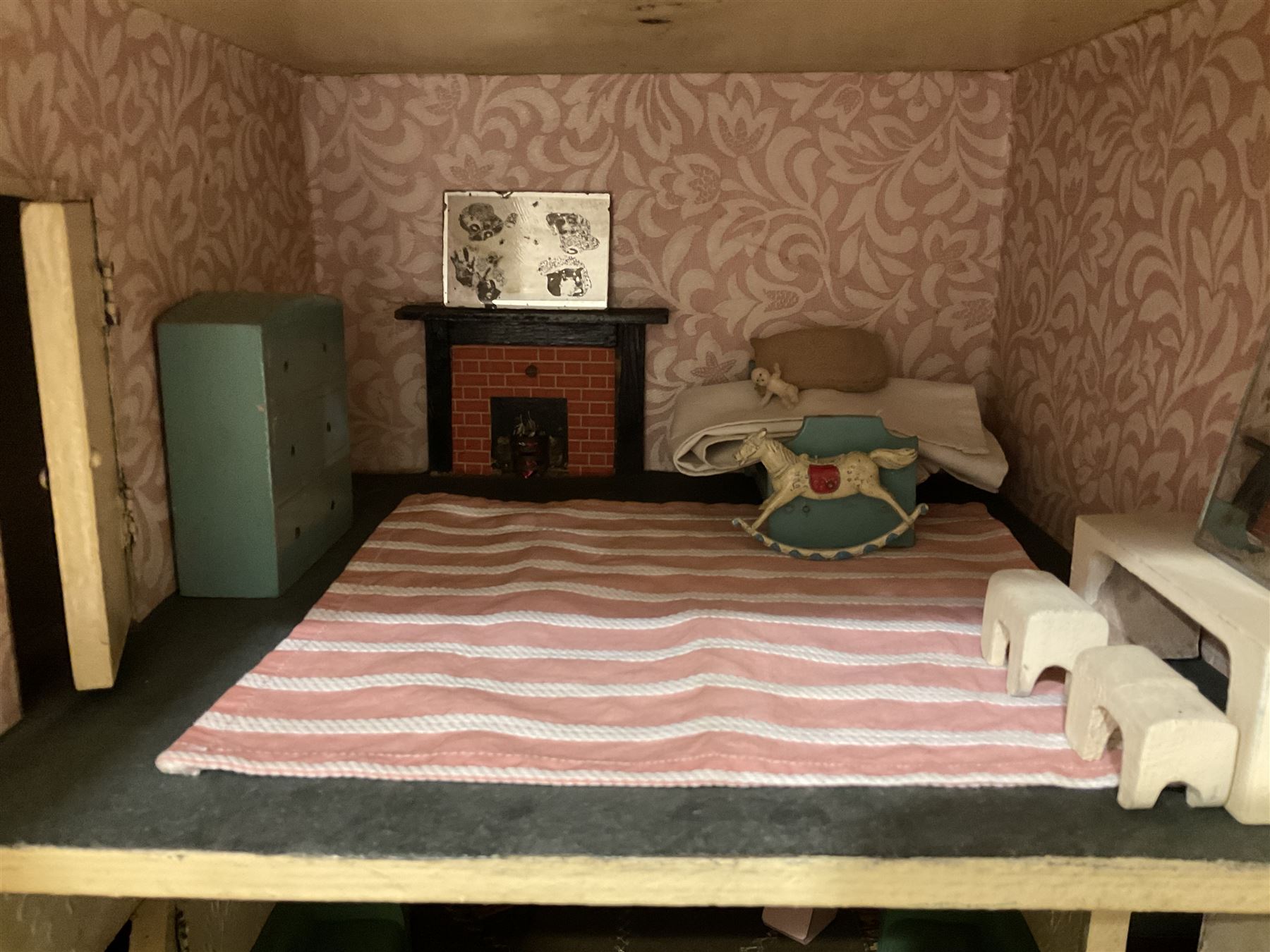 Large Tri-ang No.93 doll`s house in the 'Stockbroker's Range' c1935; two-storey double-fronted Tudor design, half timbered gables, two-storey bay windows, cream and mock shrubbery to front, opening metal framed windows with green shutters, red simulated tiled roof with chimney, integral garage with opening doors, front elevation has four hinged doors opening to reveal two bedrooms with fire places, living room, bathroom and kitchen with built in dresser and sink, entrance hall and staircase, side entrance with porch and seat and sun dial over on chimney stack; some wiring for electrical lighting; metal Tri-ang Toys disc verso; comprehensively furnished H66cm L117cm D43cm