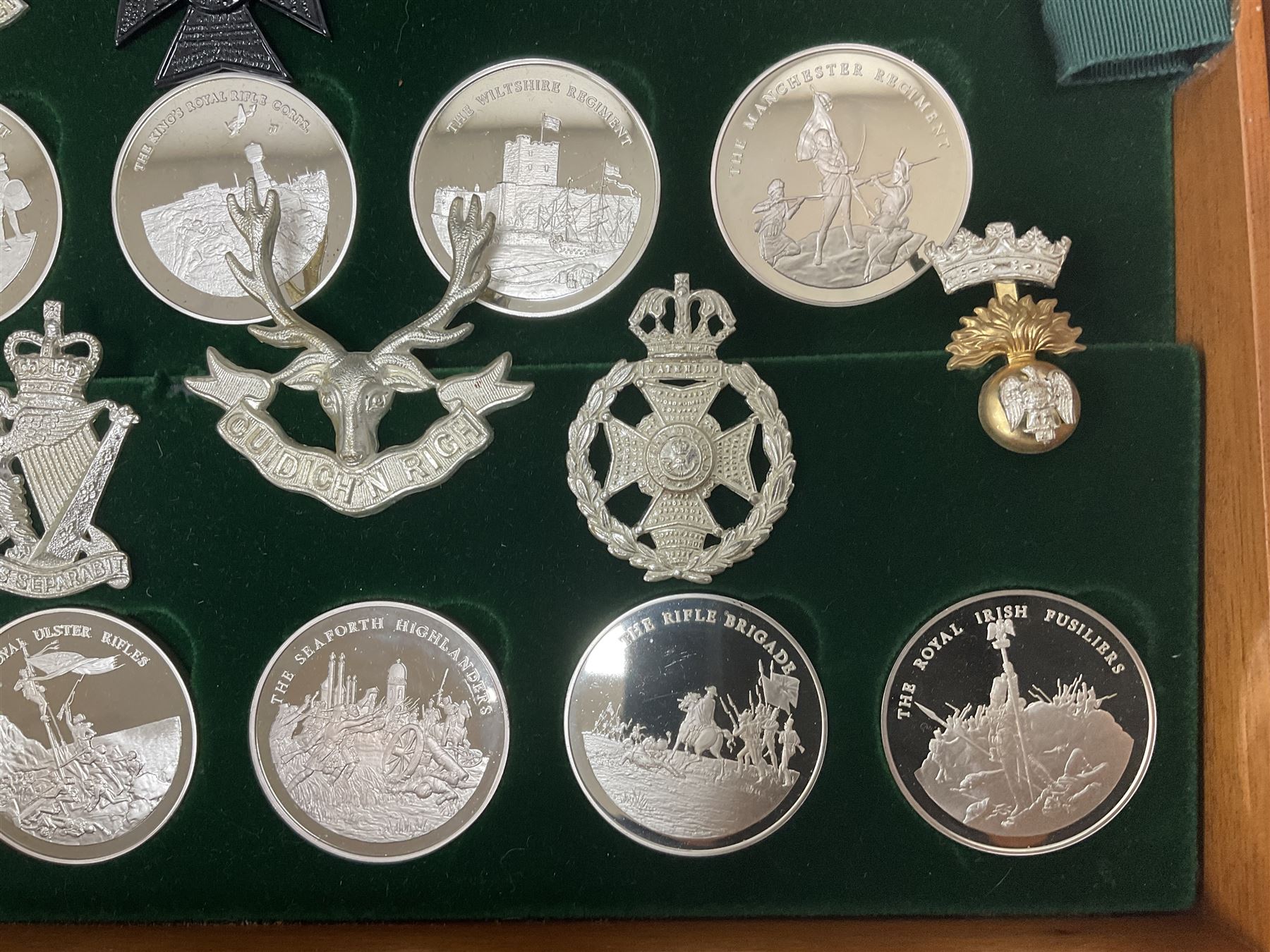 Great British Regiments, 1977, set of fifty two frosted silver medals by the Birmingham Mint, each bearing the name of a regiment with a depiction of an action on the obverse and further details on the reverse, all hallmarked Birmingham Mint, assay offices and dates; together with 52 base metal copy cap badges for each regiment, all housed and mounted on two trays and contained within a wooden presentation case, with brass plaque and fittings, lock and key, with a certificate of authenticity 