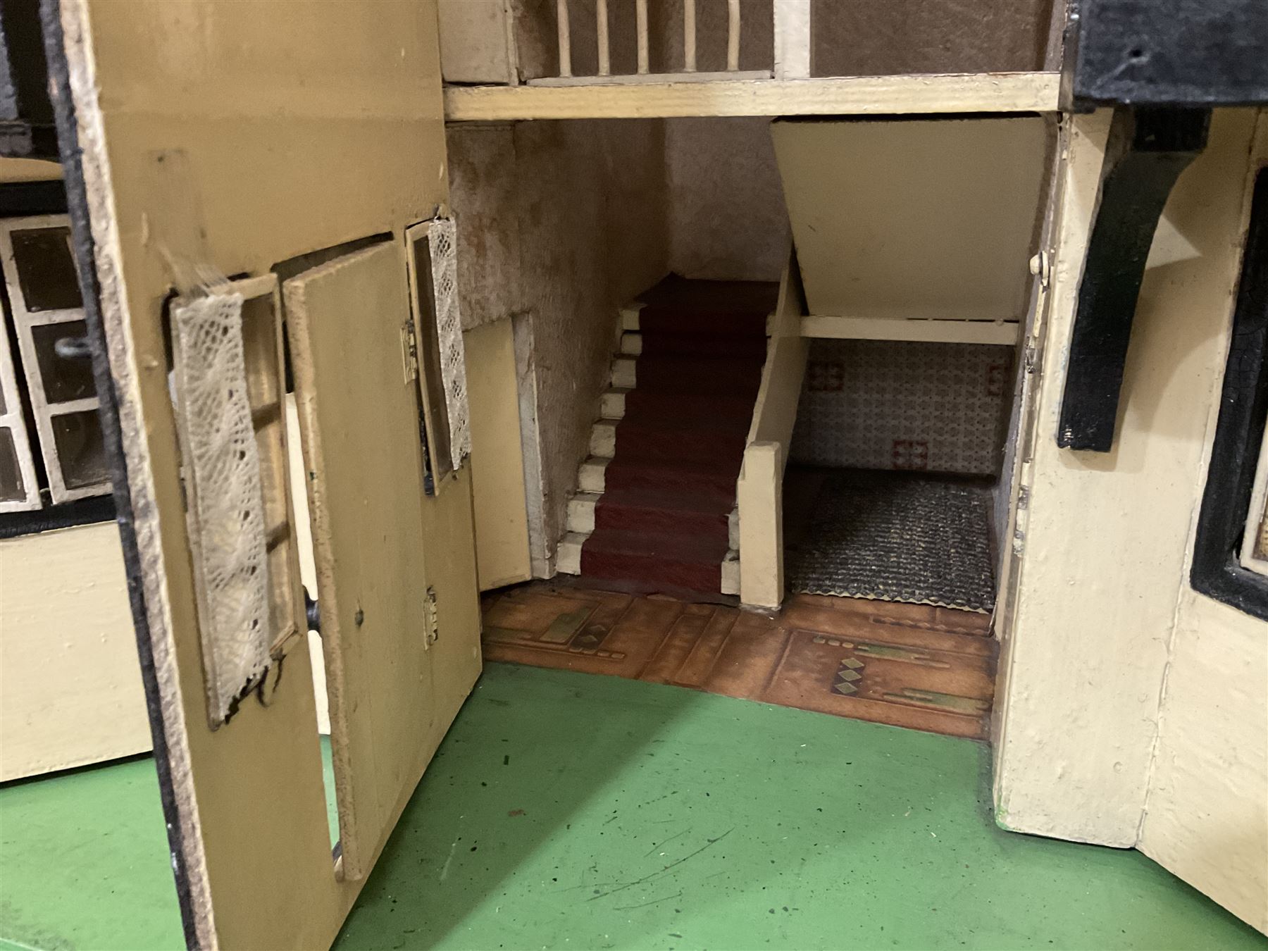 Large Tri-ang No.93 doll`s house in the 'Stockbroker's Range' c1935; two-storey double-fronted Tudor design, half timbered gables, two-storey bay windows, cream and mock shrubbery to front, opening metal framed windows with green shutters, red simulated tiled roof with chimney, integral garage with opening doors, front elevation has four hinged doors opening to reveal two bedrooms with fire places, living room, bathroom and kitchen with built in dresser and sink, entrance hall and staircase, side entrance with porch and seat and sun dial over on chimney stack; some wiring for electrical lighting; metal Tri-ang Toys disc verso; comprehensively furnished H66cm L117cm D43cm