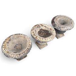 Set of three 19th century weathered carved sandstone garden urns of Neoclassical campana form, the broad everted rim carved with pointed egg-and-dart motifs, above a plain waisted bowl with gadrooned underbelly, on moulded rope-twist socle and square plinth base