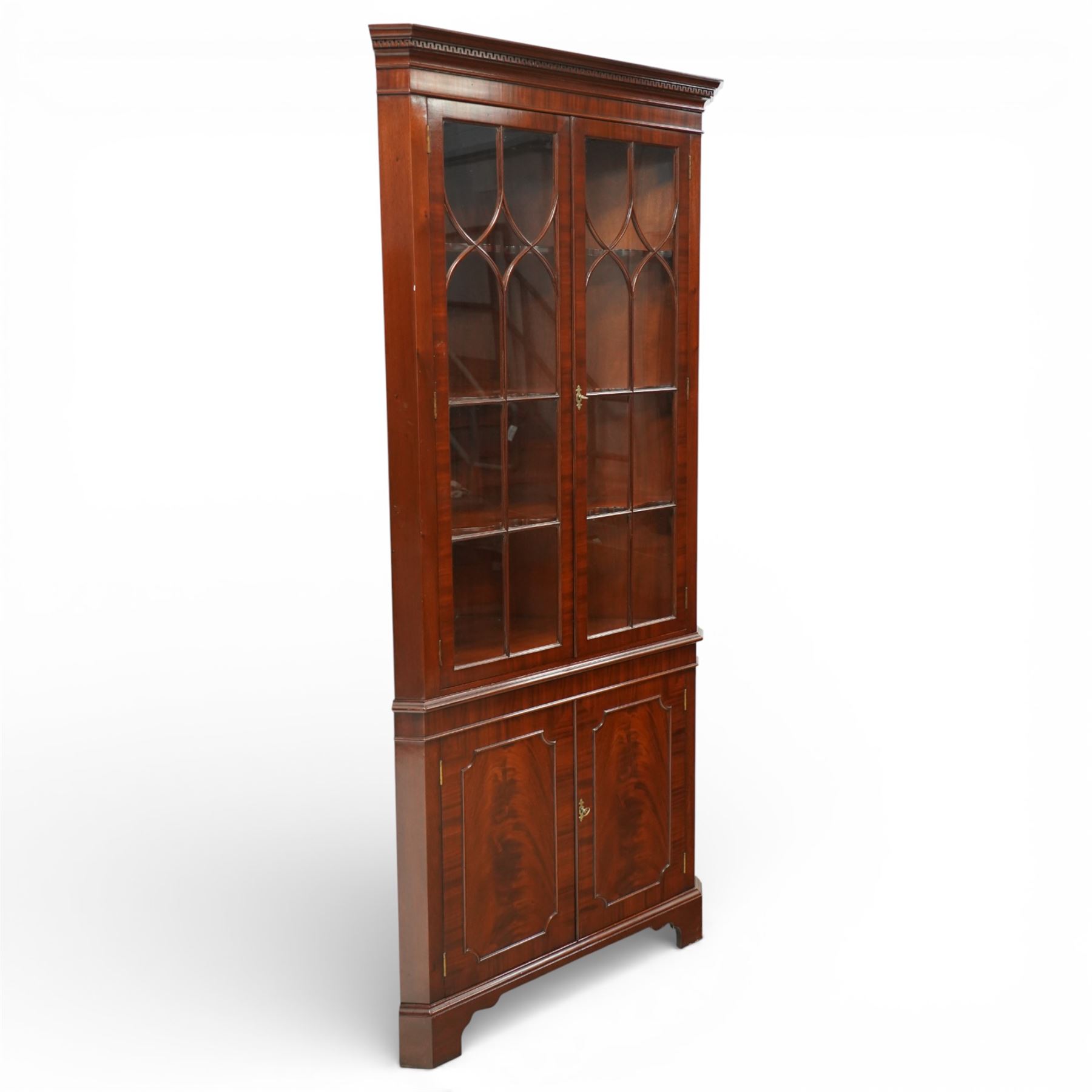 William Tillman - Early 20th century mahogany corner cabinet, the projecting moulded cornice with dentil detail over a glazed upper section enclosed by a pair of astragal glazed doors with Gothic arched tracery, the interior fitted with shaped shelves, above a moulded waist and a lower cupboard enclosed by two panelled doors with shaped fielded panels, raised on bracket feet