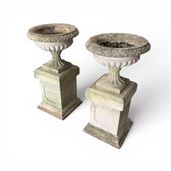 Pair of weathered cast stone Neoclassical design garden Kylix shape urns, foliate moulded rim over a gadrooned underbelly, the scalloped socle over a rectangular pedestal with faux-panelled sides, stamped with stylised ‘H’ monogram